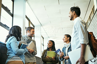 Buy stock photo Low angle shot of a group of university students talking while standing in a campus corridor