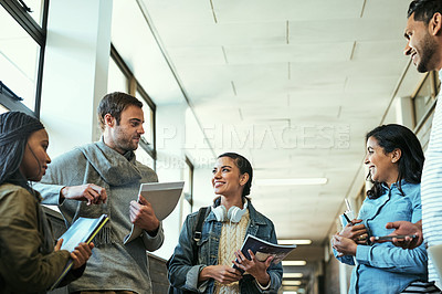 Buy stock photo Low angle shot of a group of university students talking while standing in a campus corridor