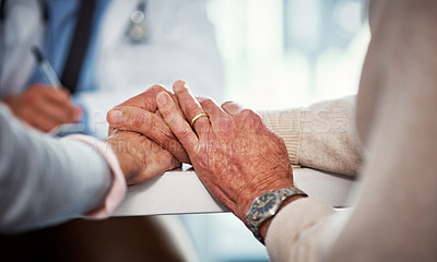 Buy stock photo Closeup shot of a senior couple holding hands in comfort while consulting a doctor in a clinic