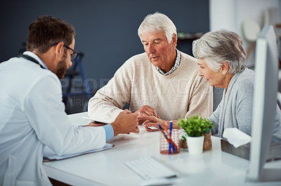 Buy stock photo Shot of a doctor discussing something on a digital tablet with a senior couple in a clinic