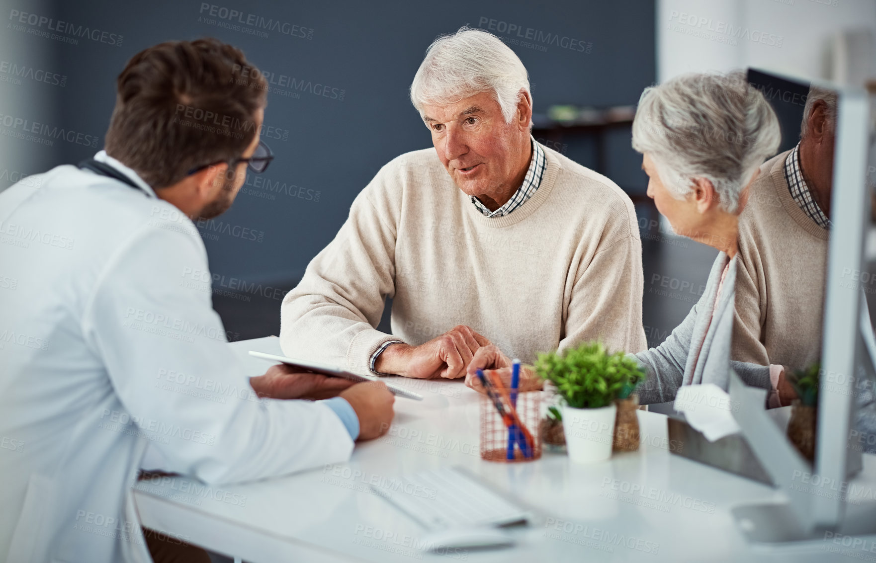 Buy stock photo Shot of a doctor discussing something on a digital tablet with a senior couple in a clinic