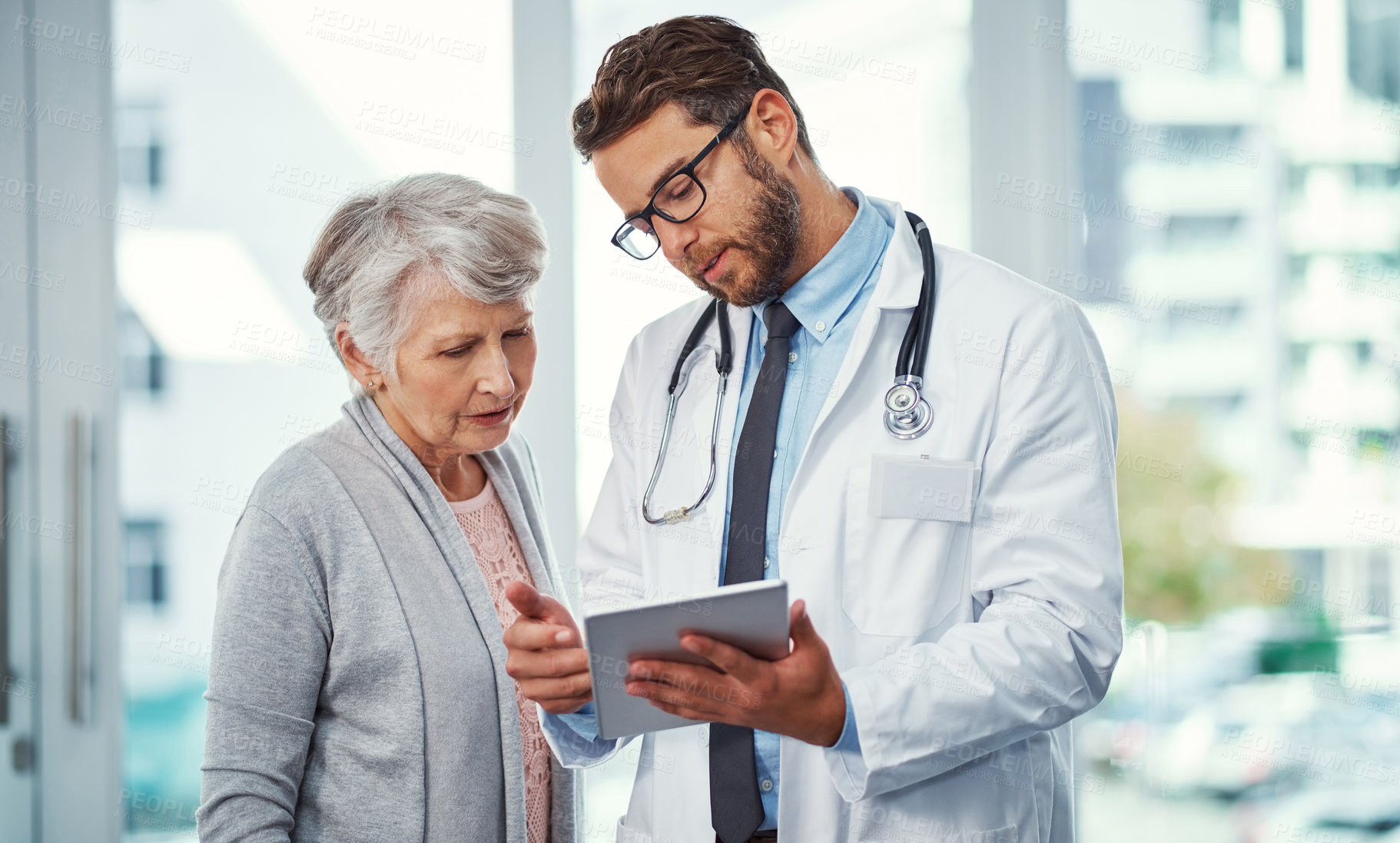 Buy stock photo Shot of a doctor discussing something on a digital tablet with a senior patient in a clinic