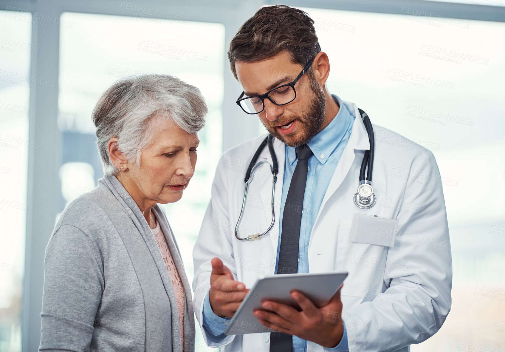 Buy stock photo Shot of a doctor discussing something on a digital tablet with a senior patient in a clinic