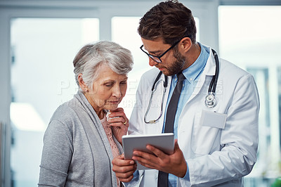 Buy stock photo Shot of a doctor discussing something on a digital tablet with a senior patient in a clinic
