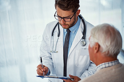 Buy stock photo Shot of a doctor writing notes while examining a senior patient in a clinic