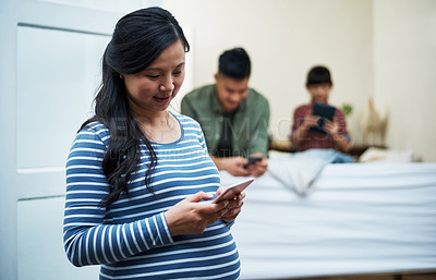 Buy stock photo Shot of a pregnant woman using a digital tablet with her family in the background