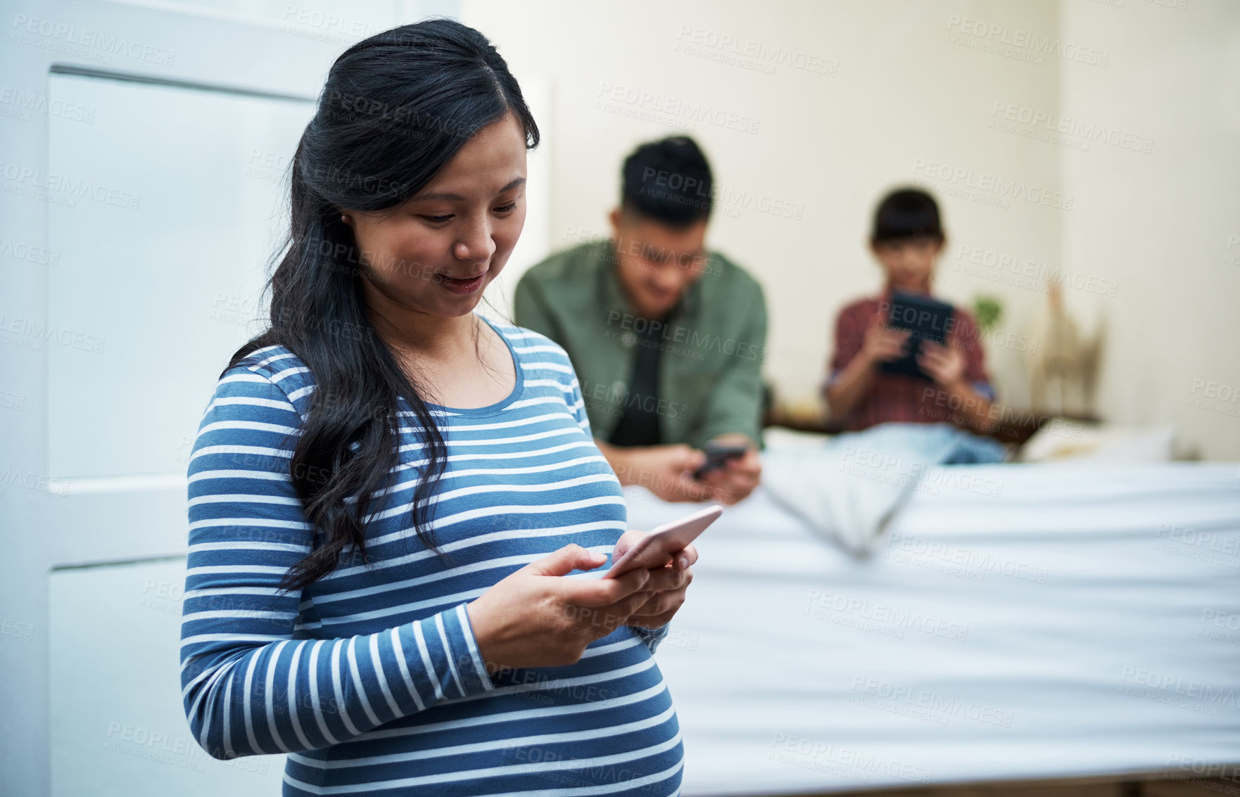 Buy stock photo Shot of a pregnant woman using a digital tablet with her family in the background