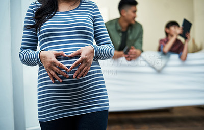 Buy stock photo Shot of a pregnant woman making a heart shape with her hands on her stomach at home