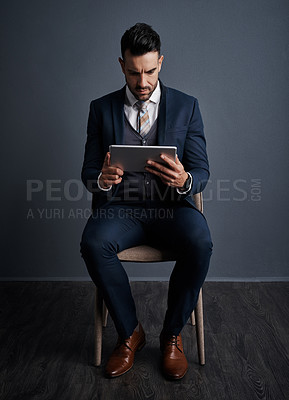 Buy stock photo Studio shot of a stylish young businessman using a digital tablet against a gray background