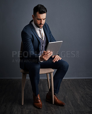 Buy stock photo Studio shot of a stylish young businessman using a digital tablet against a gray background
