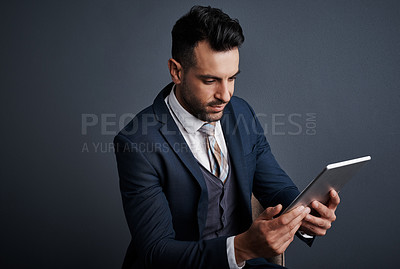 Buy stock photo Studio shot of a stylish young businessman using a digital tablet against a gray background