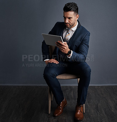 Buy stock photo Studio shot of a stylish young businessman using a digital tablet against a gray background
