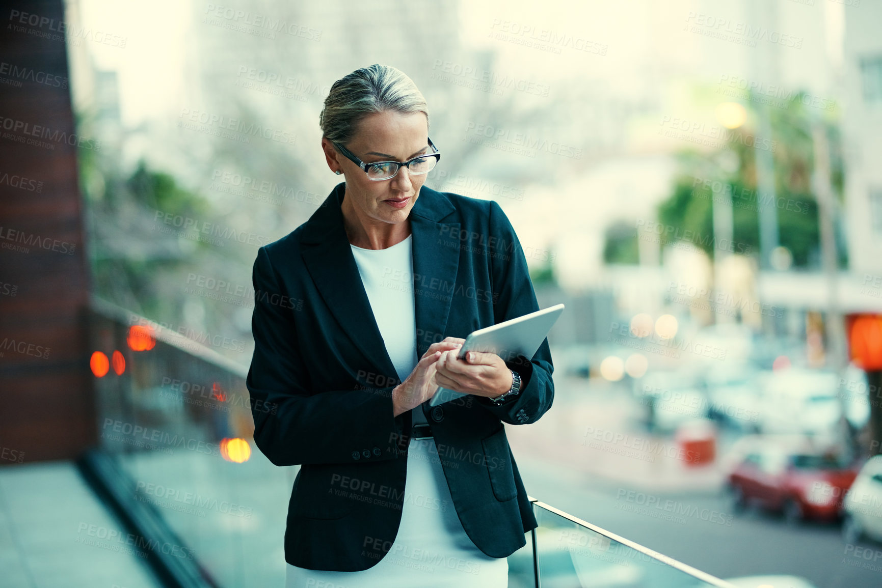 Buy stock photo Shot of a mature businesswoman standing outside on the balcony of an office and using a digital tablet