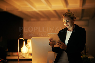 Buy stock photo Shot of a mature woman using her digital tablet while working late at the office
