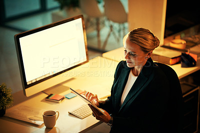 Buy stock photo Shot of a mature woman using her digital tablet while working late at the office