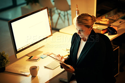 Buy stock photo Shot of a mature woman using her digital tablet while working late at the office