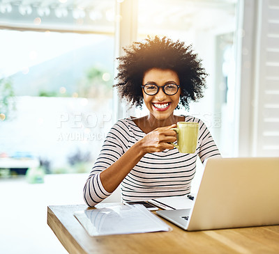 Buy stock photo Portrait of a cheerful young woman working on a laptop and drinking coffee while looking at the camera at home