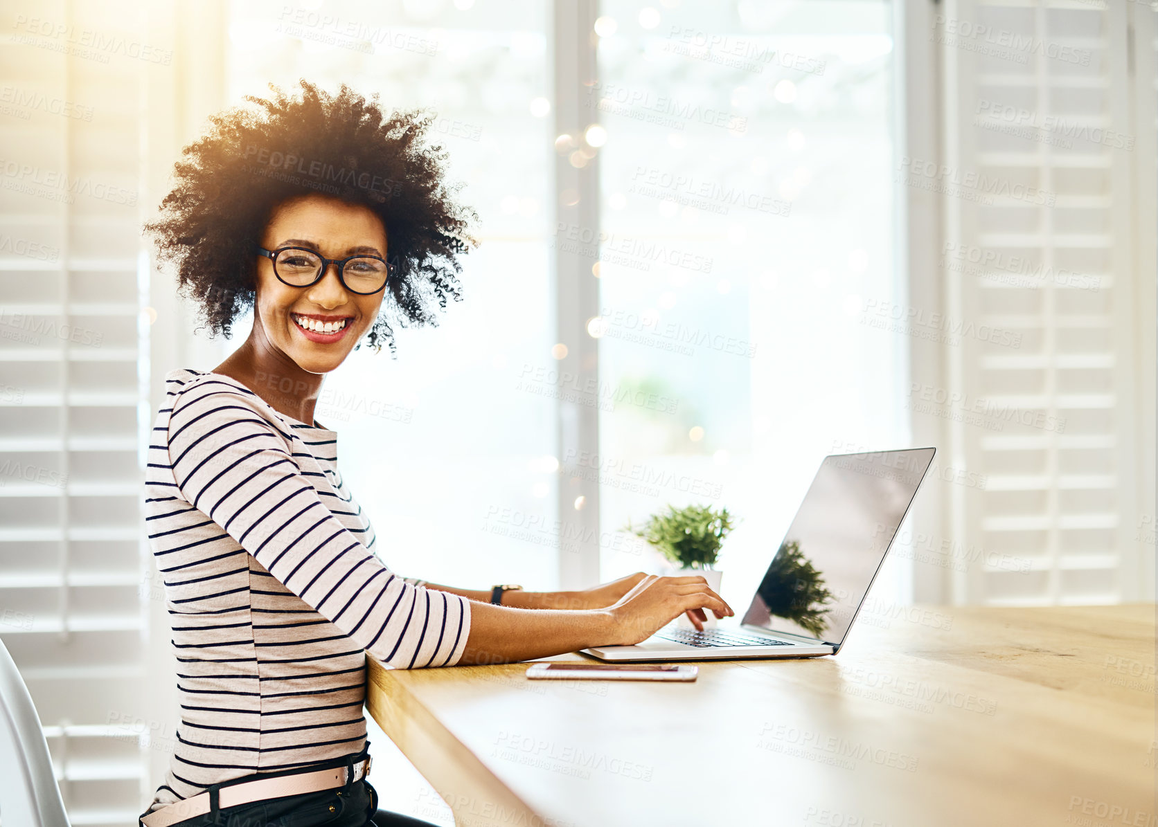 Buy stock photo Portrait of a cheerful young woman working on her laptop while looking at the camera