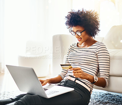 Buy stock photo Shot of a cheerful young woman doing online shopping on her laptop while being seated on the floor at home