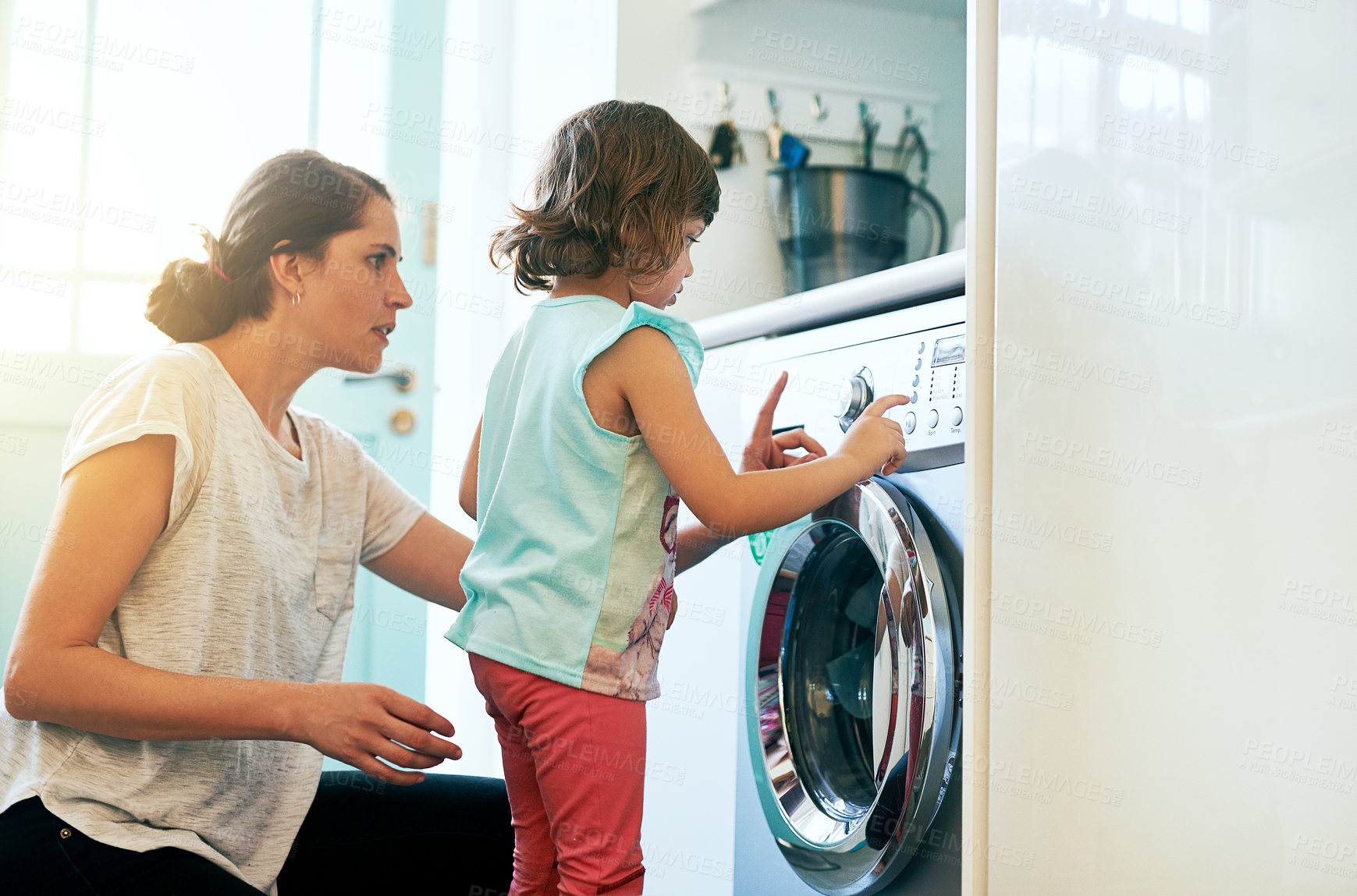 Buy stock photo Help, home and mom with girl at washing machine for chores, teaching and learning housekeeping routine. Laundry, mother and daughter cleaning clothes together with support, care and child development