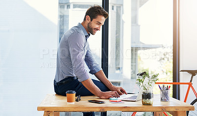 Buy stock photo Shot of a handsome young businessman using his laptop in his office