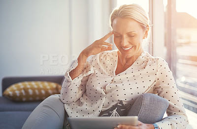 Buy stock photo Cropped shot of a mature woman using her digital tablet while relaxing at home