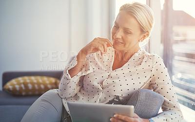 Buy stock photo Cropped shot of a mature woman using her digital tablet while relaxing at home