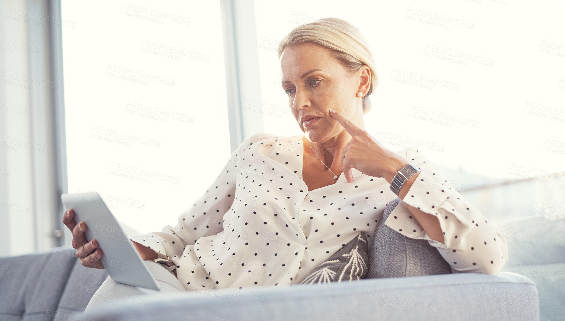 Buy stock photo Cropped shot of a mature woman using her digital tablet while relaxing at home