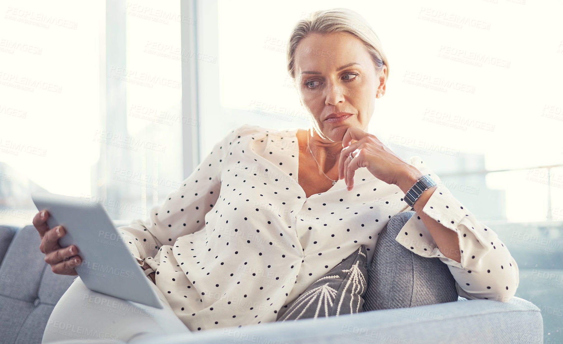 Buy stock photo Cropped shot of a mature woman using her digital tablet while relaxing at home