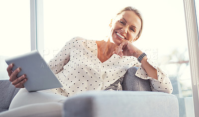 Buy stock photo Cropped shot of a mature woman using her digital tablet while relaxing at home