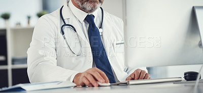 Buy stock photo Cropped shot of a mature doctor using a computer at a desk in his office