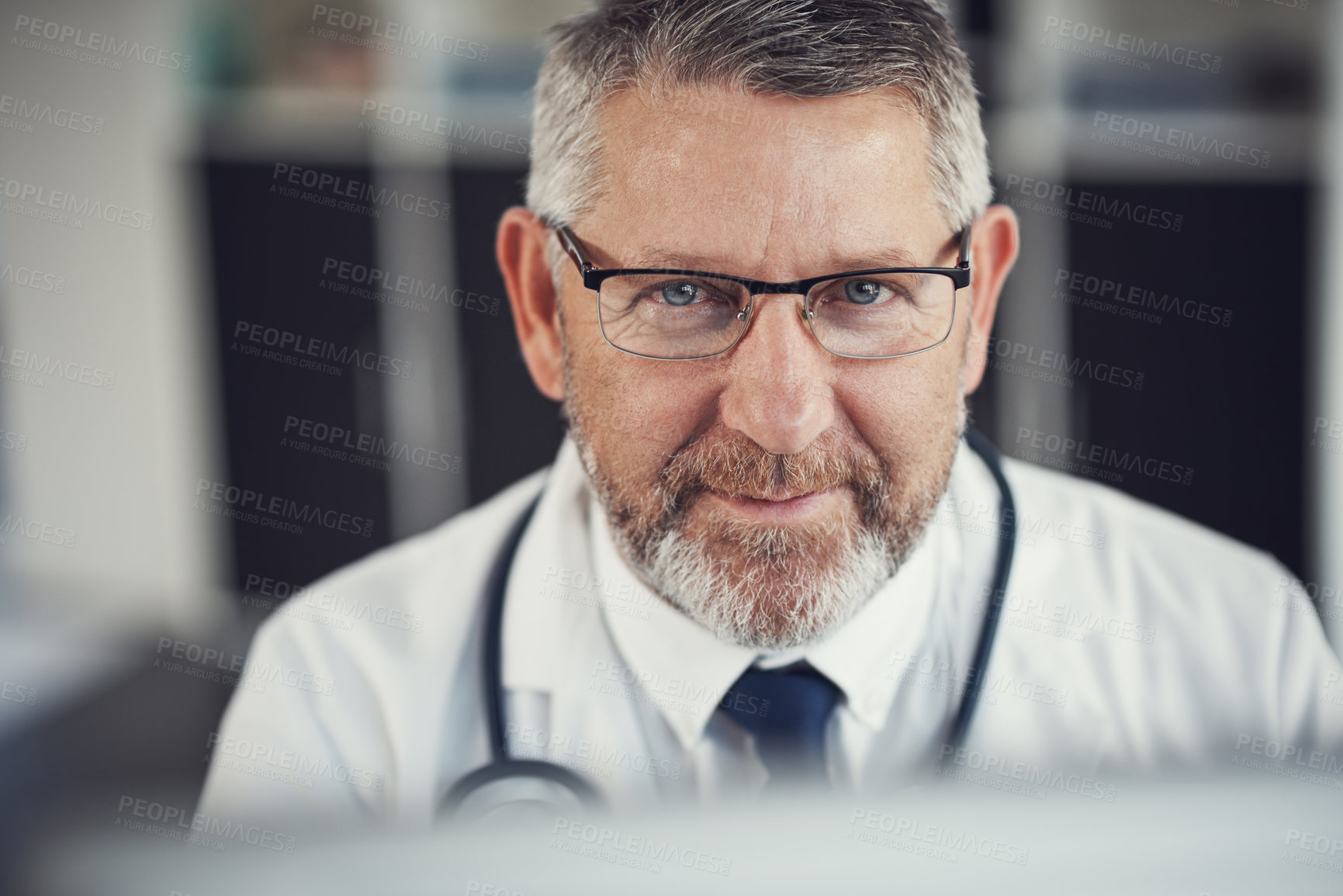 Buy stock photo Portrait of a mature doctor using a computer at a desk in his office