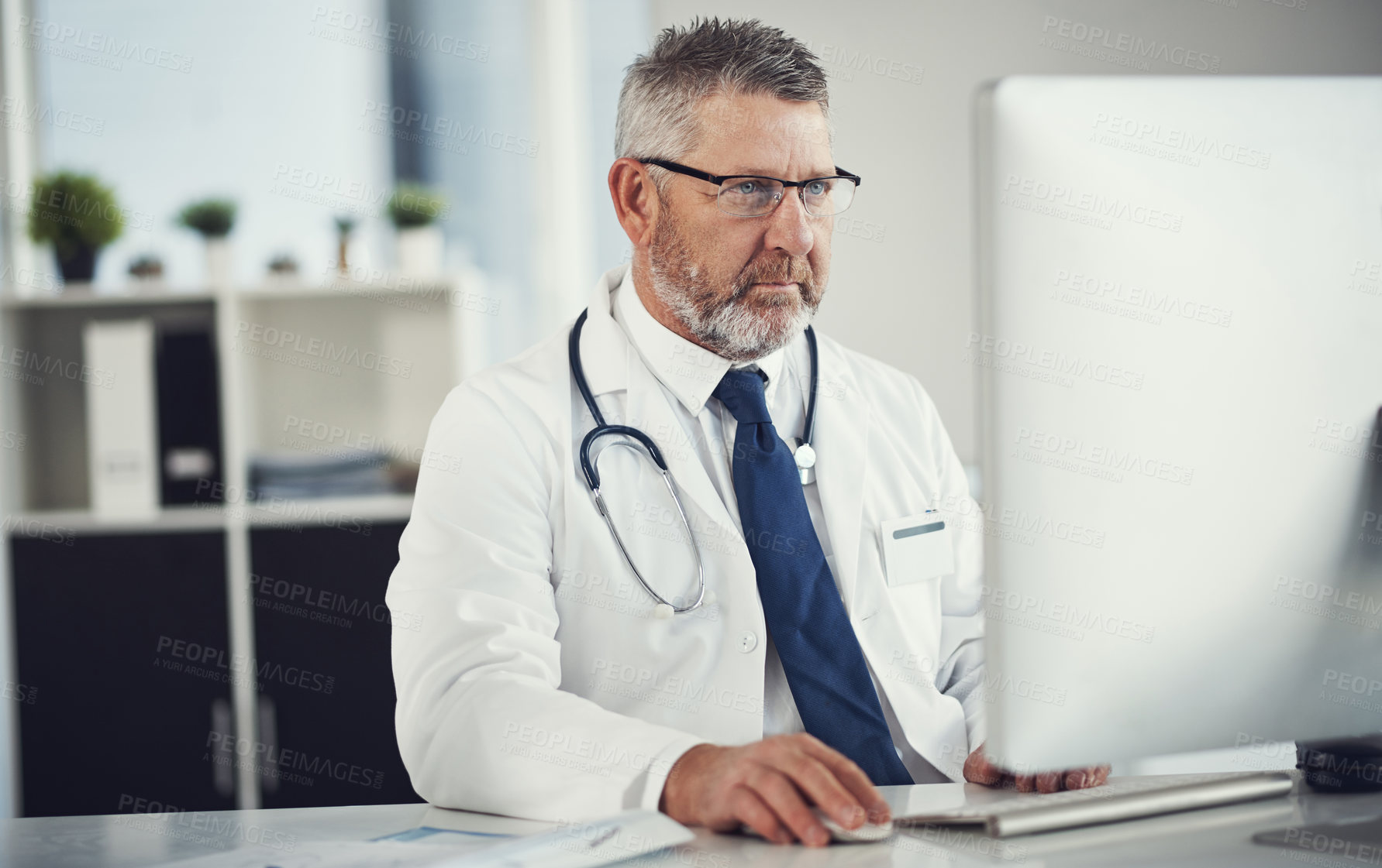 Buy stock photo Shot of a mature doctor using a computer at a desk in his office