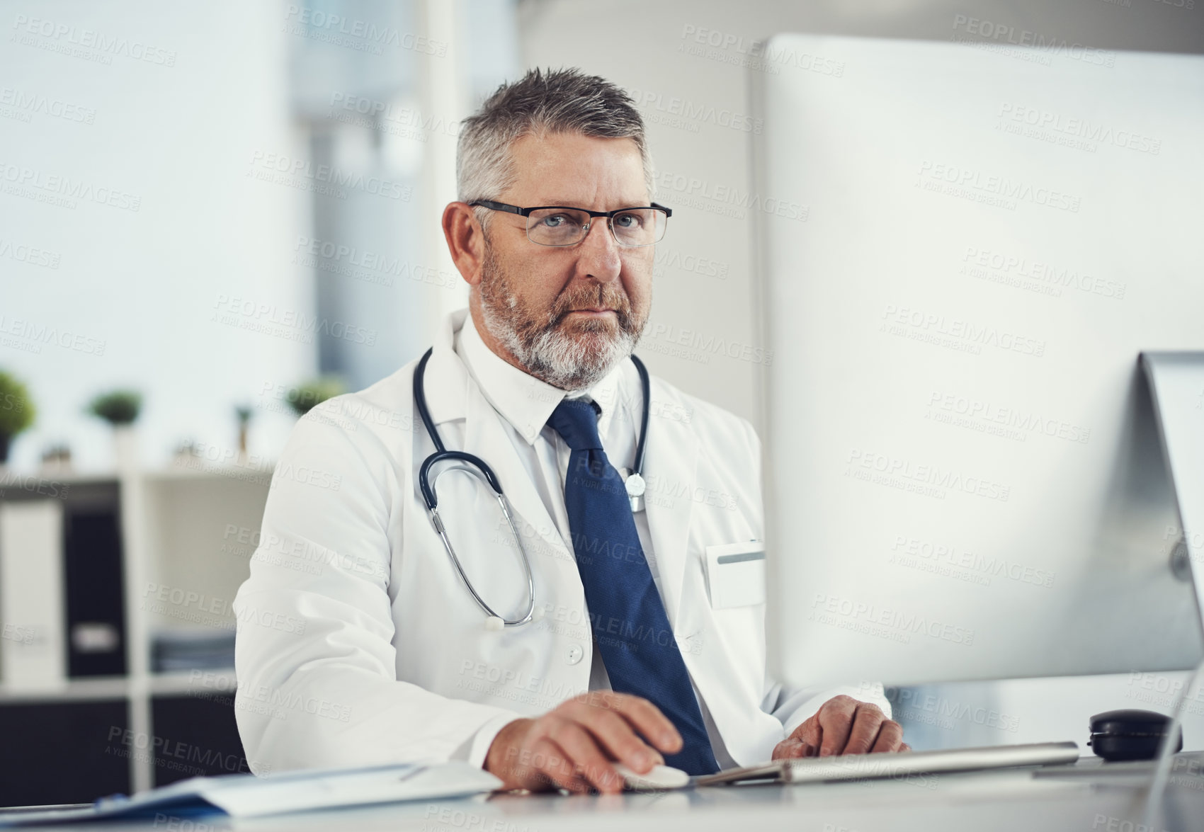 Buy stock photo Portrait of a mature doctor using a computer at a desk in his office