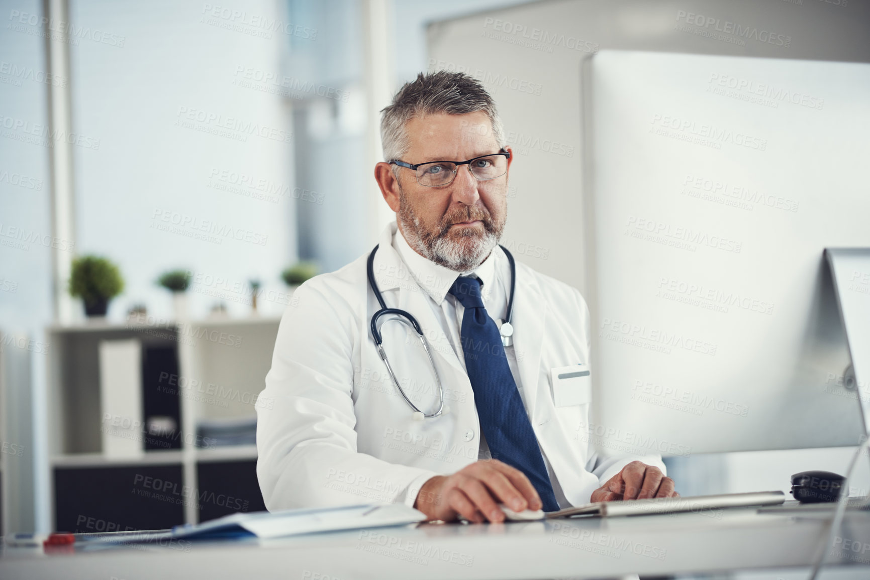 Buy stock photo Portrait of a mature doctor using a computer at a desk in his office