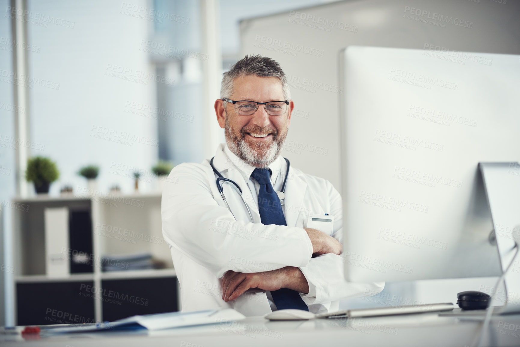 Buy stock photo Portrait of a mature doctor using a computer at a desk in his office