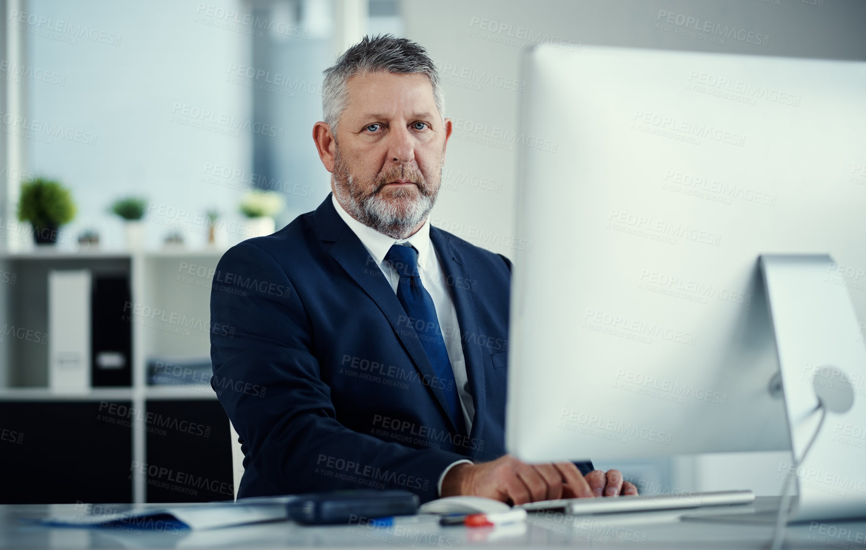 Buy stock photo Portrait of a mature businessman using a computer at his desk in a modern office