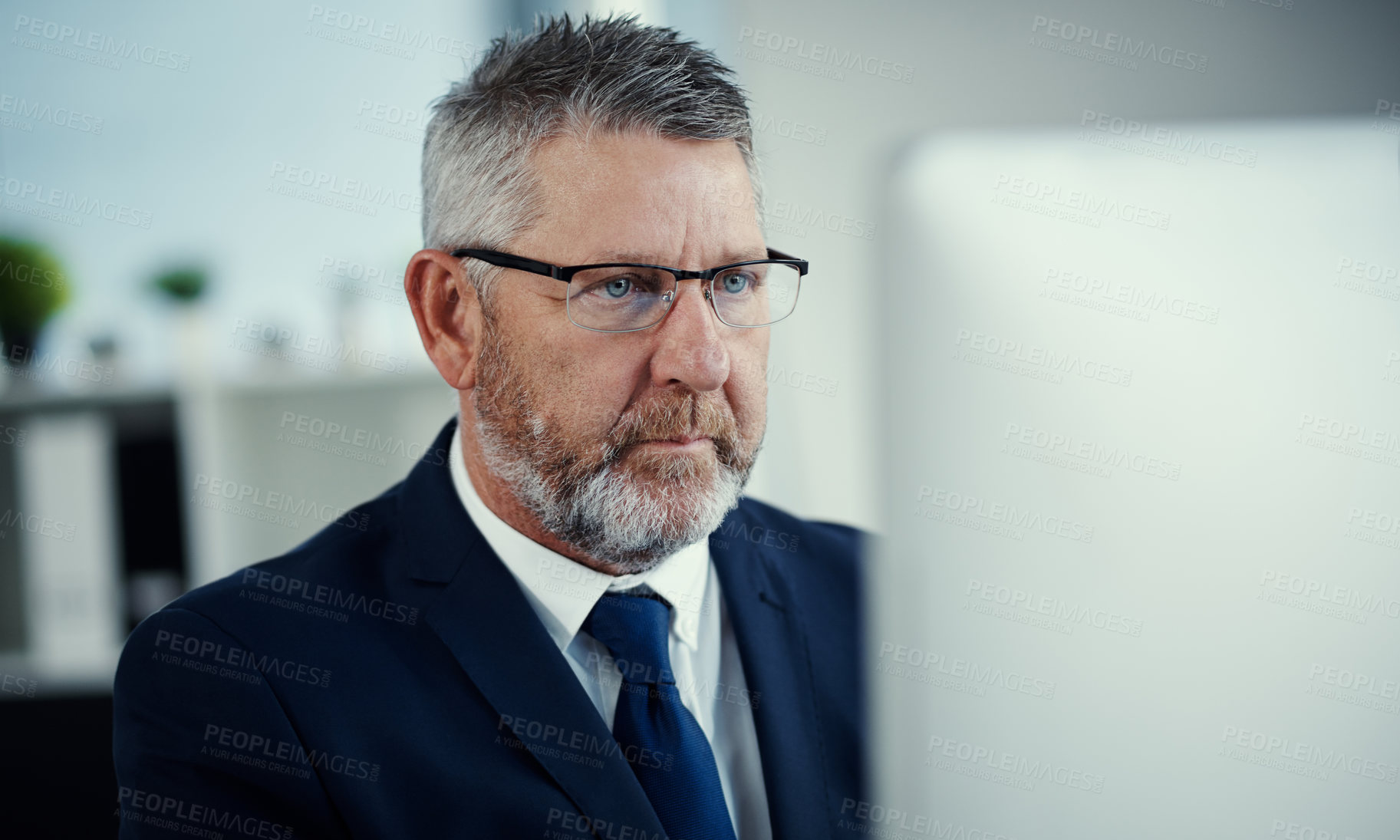 Buy stock photo Shot of a mature businessman using a computer at his desk in a modern office