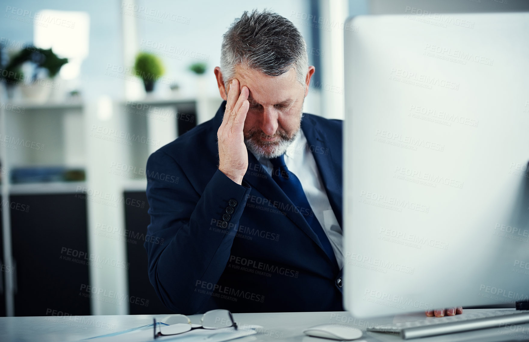 Buy stock photo Shot of a mature businessman experiencing a headache while working at his desk in a modern office