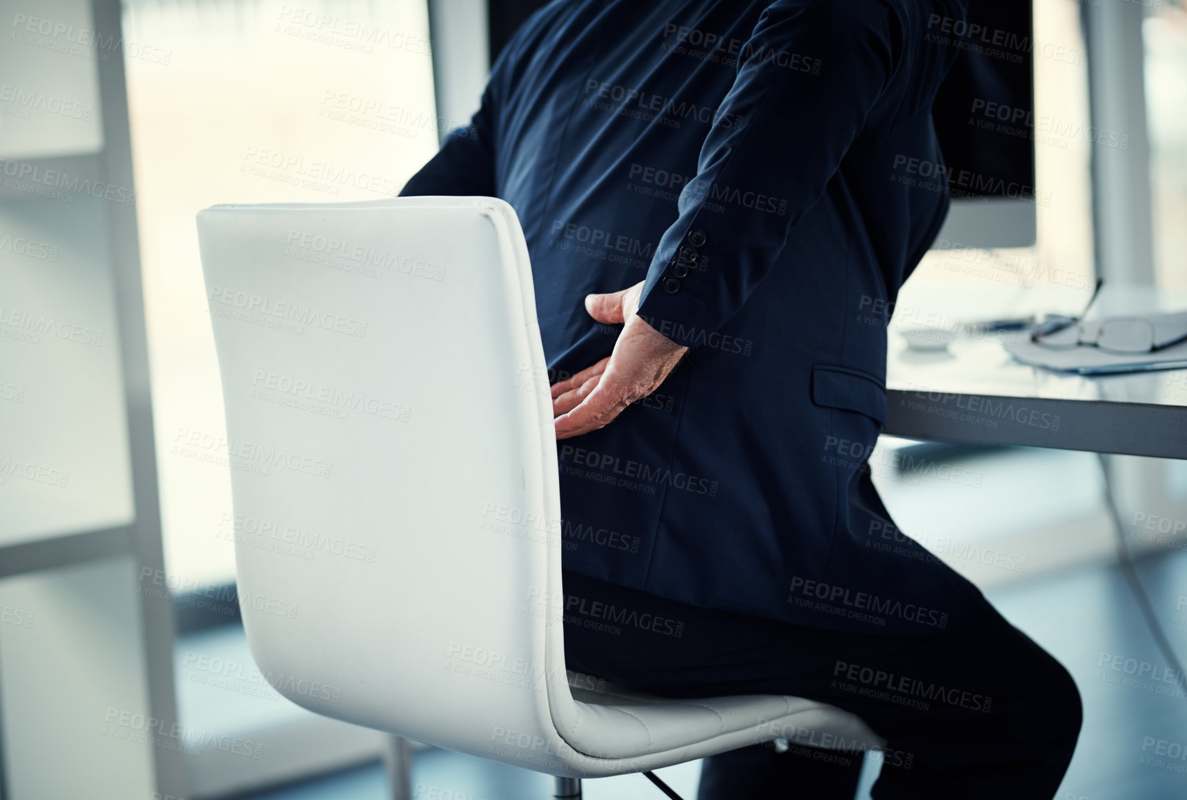 Buy stock photo Cropped shot of a businessman experiencing back ache while working at his desk