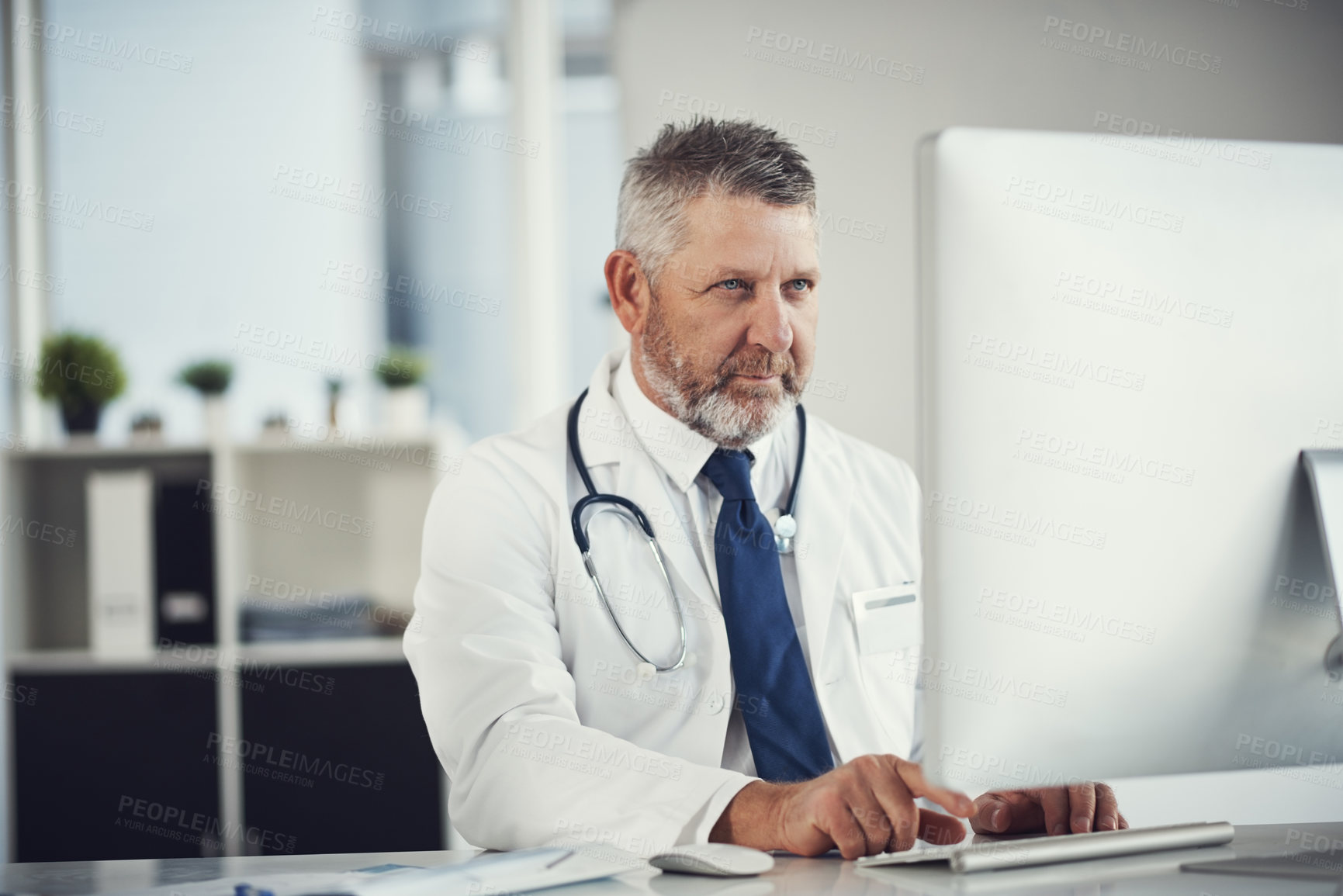 Buy stock photo Shot of a mature doctor using a computer at a desk in his office