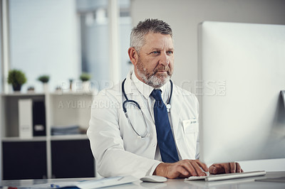 Buy stock photo Shot of a mature doctor using a computer at a desk in his office