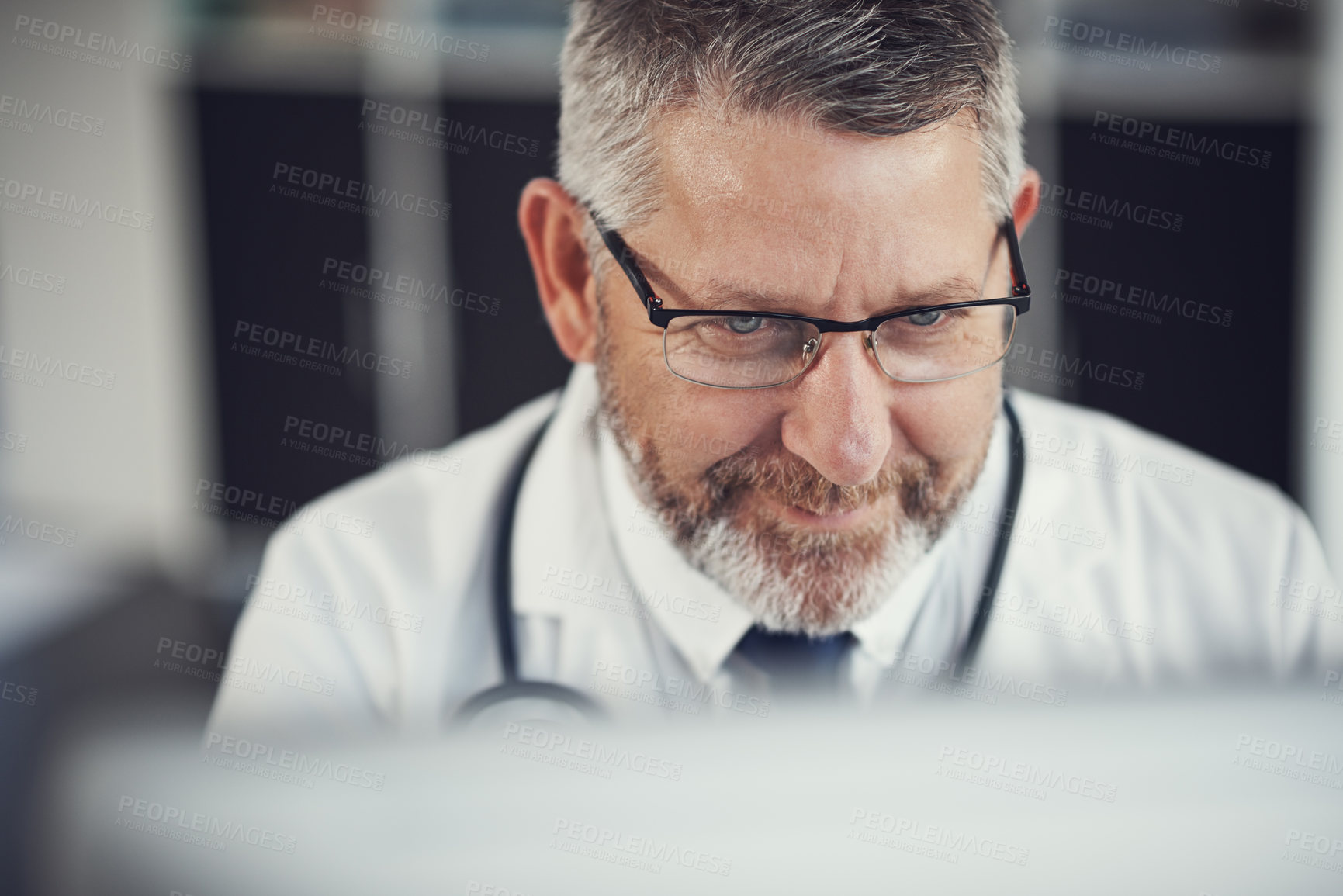 Buy stock photo Shot of a mature doctor using a computer at a desk in his office