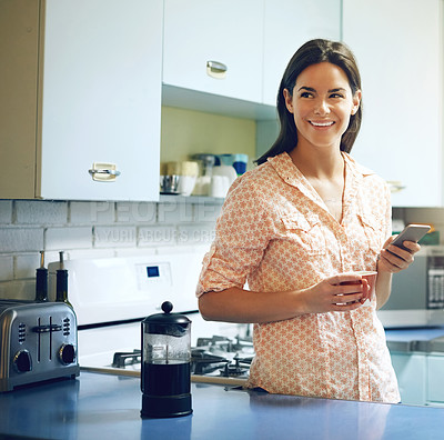 Buy stock photo Shot of an attractive young woman having coffee and using a mobile phone at home