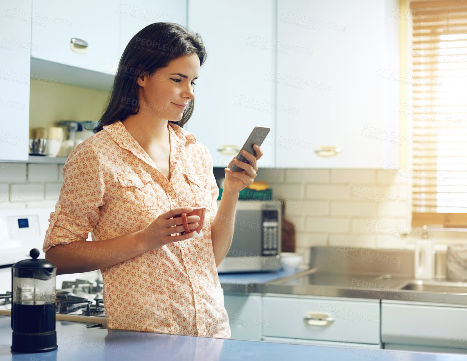 Buy stock photo Shot of an attractive young woman having coffee and using a mobile phone at home