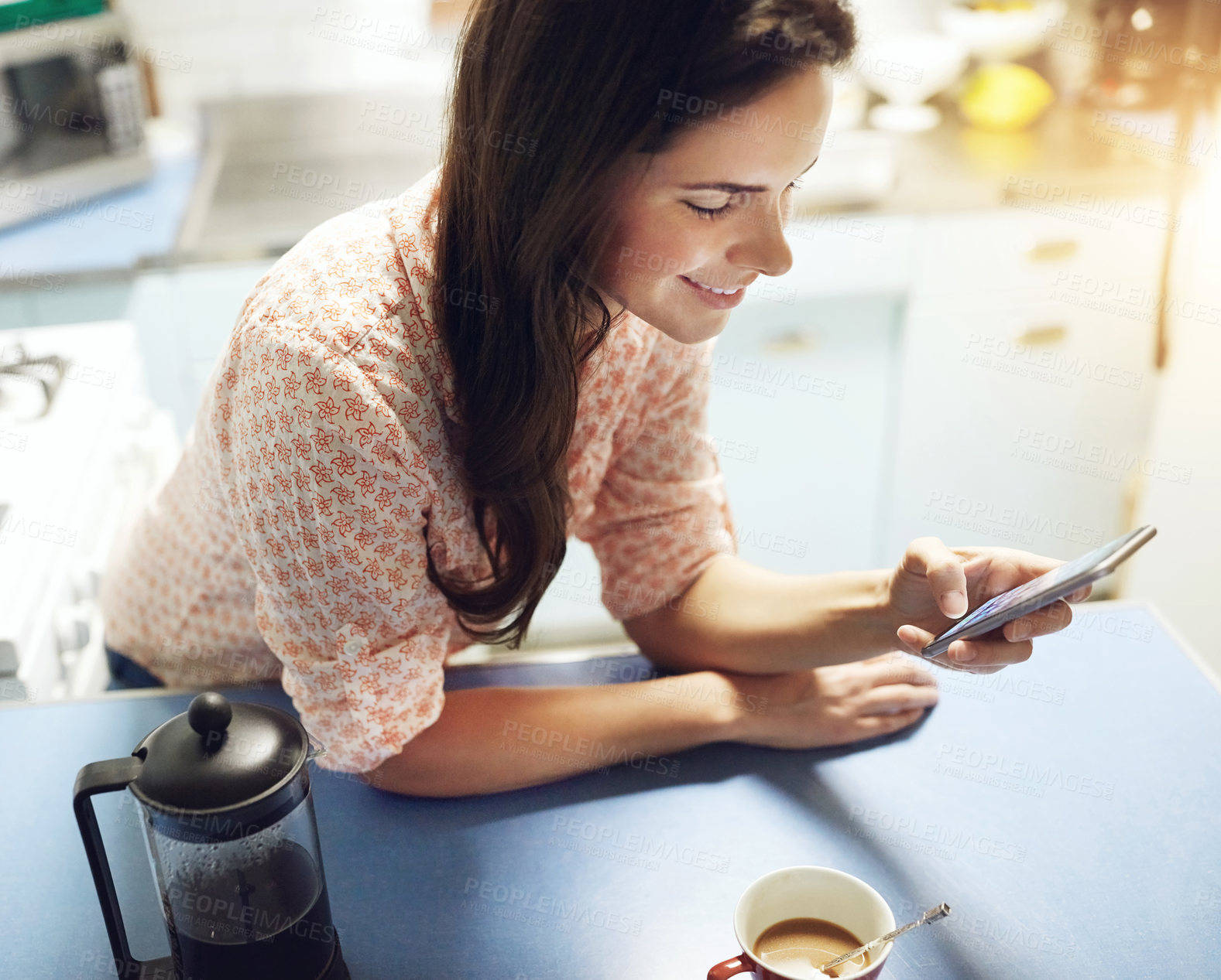 Buy stock photo Shot of an attractive young woman having coffee and using a mobile phone at home