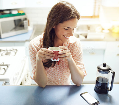 Buy stock photo Shot of an attractive young woman having coffee and looking at her mobile phone at home