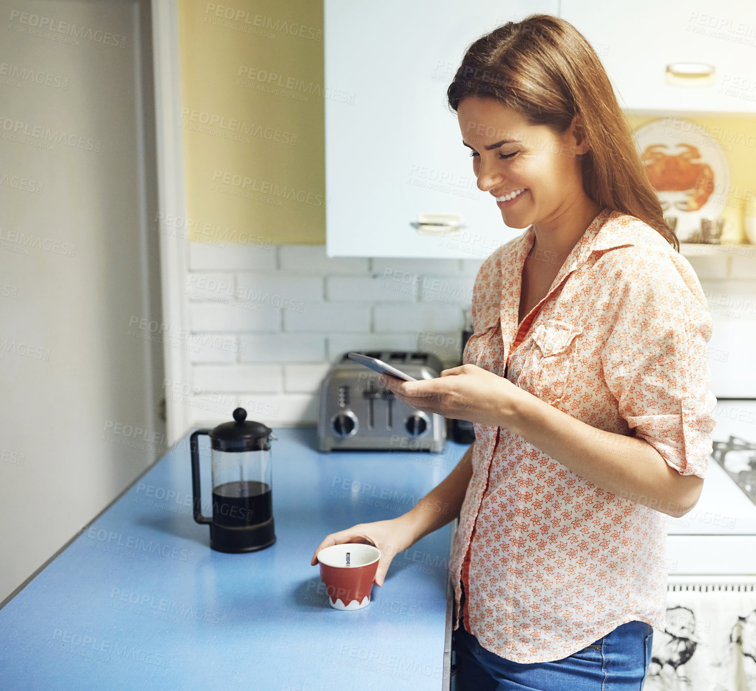 Buy stock photo Shot of an attractive young woman having coffee and using a mobile phone at home