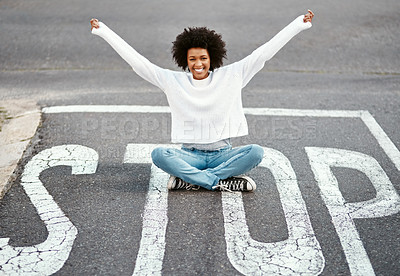Buy stock photo Portrait of a happy young woman sitting on a stop sign at an intersection