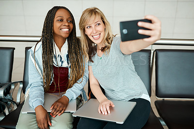 Buy stock photo Cropped shot of two young girlfriends taking selfies in the departure lounge of an airport